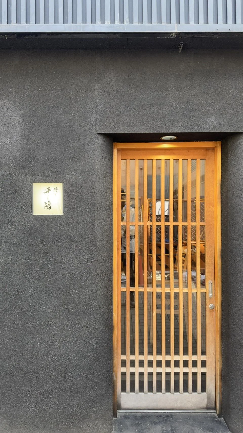 鮨 千陽の玄関。黒い外壁と木の格子戸、左手に千陽の看板。